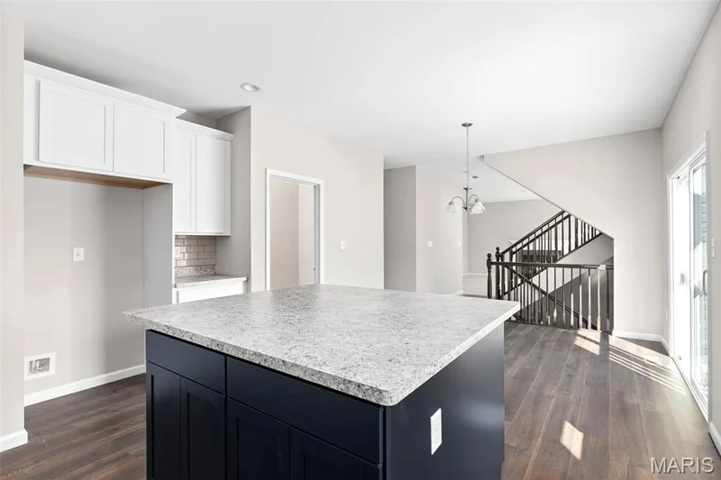 Kitchen with baseboards, a kitchen island, dark wood-style flooring, white cabinets, and light countertops — 2 Hermitage II at Harvest Estate, O'Fallon, MO 63368