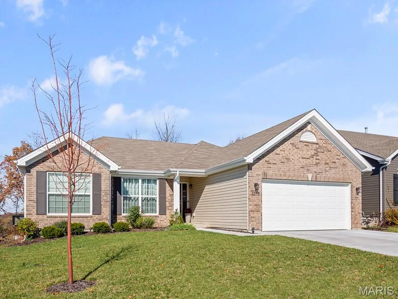 Ranch-style house featuring brick siding, a garage, concrete driveway, a front lawn, and a shingled roof — 2 Hickory at Harvest Estates, O'Fallon, MO 63368