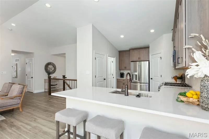 Kitchen featuring stainless steel refrigerator with ice dispenser, a peninsula, a sink, light wood-style floors, and vaulted ceiling — 2 Hickory at Harvest Estates, O'Fallon, MO 63368