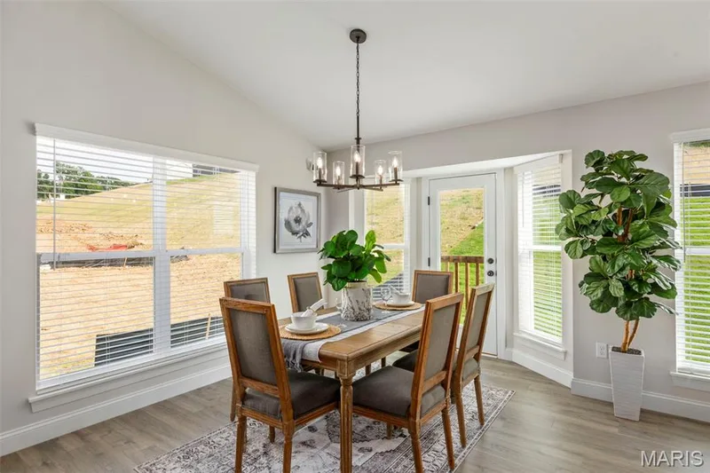 Dining area featuring a chandelier, plenty of natural light, baseboards, lofted ceiling, and wood finished floors — 2 Hickory at Harvest Estates, O'Fallon, MO 63368