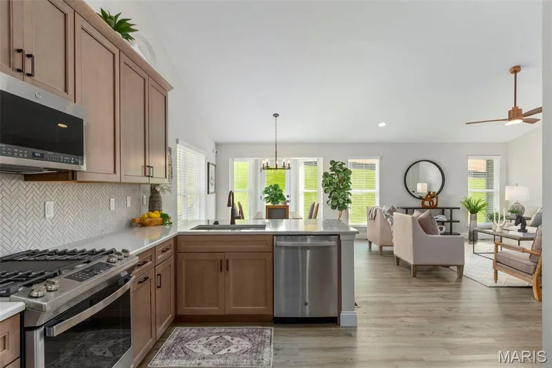 Kitchen featuring appliances with stainless steel finishes, a sink, a peninsula, light wood-type flooring, and light countertops — 2 Hickory at Harvest Estates, O'Fallon, MO 63368