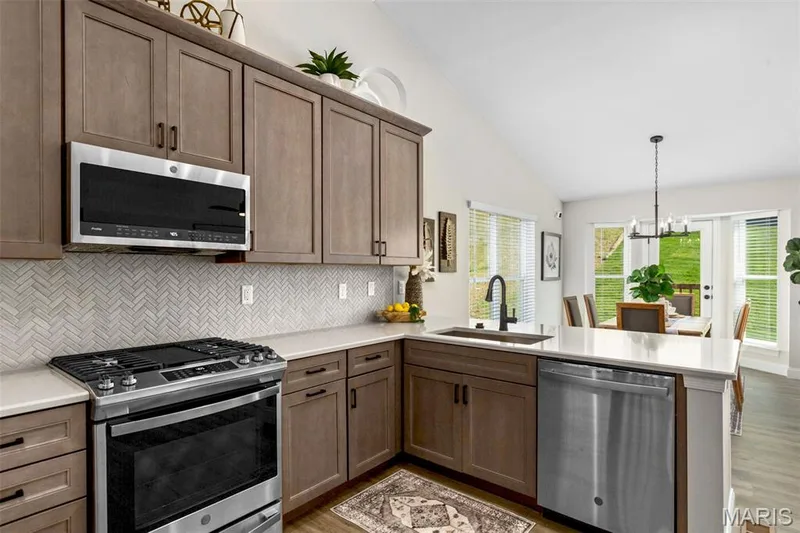 Kitchen with appliances with stainless steel finishes, a peninsula, a sink, lofted ceiling, and light wood-type flooring — 2 Hickory at Harvest Estates, O'Fallon, MO 63368