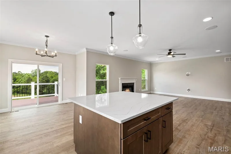 Kitchen featuring open floor plan, a warm lit fireplace, light wood-type flooring, baseboards, and recessed lighting — 2 Maple Expanded at Harvest Est, O'Fallon, MO 63385