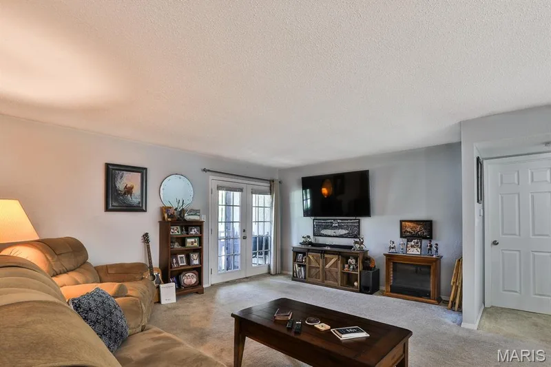 Living room featuring a textured ceiling, light colored carpet, and french doors — 1380 Heritage Landing #206, St Charles, MO 63303