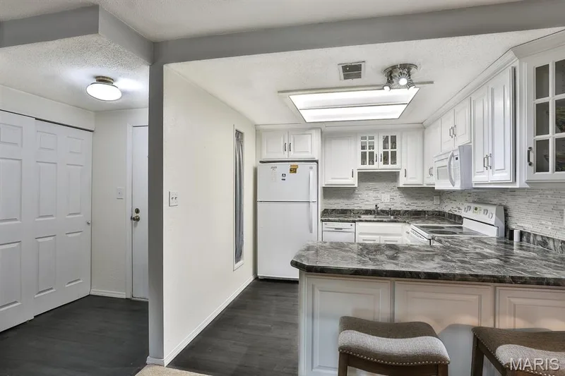 Kitchen with white appliances, a peninsula, decorative backsplash, a textured ceiling, and glass insert cabinets — 1380 Heritage Landing #206, St Charles, MO 63303