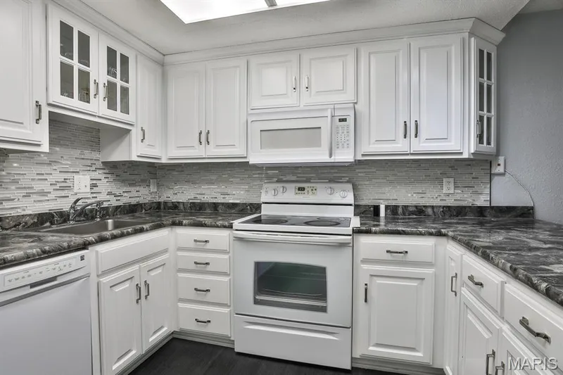 Kitchen with white appliances, white cabinetry, backsplash, and glass insert cabinets — 1380 Heritage Landing #206, St Charles, MO 63303