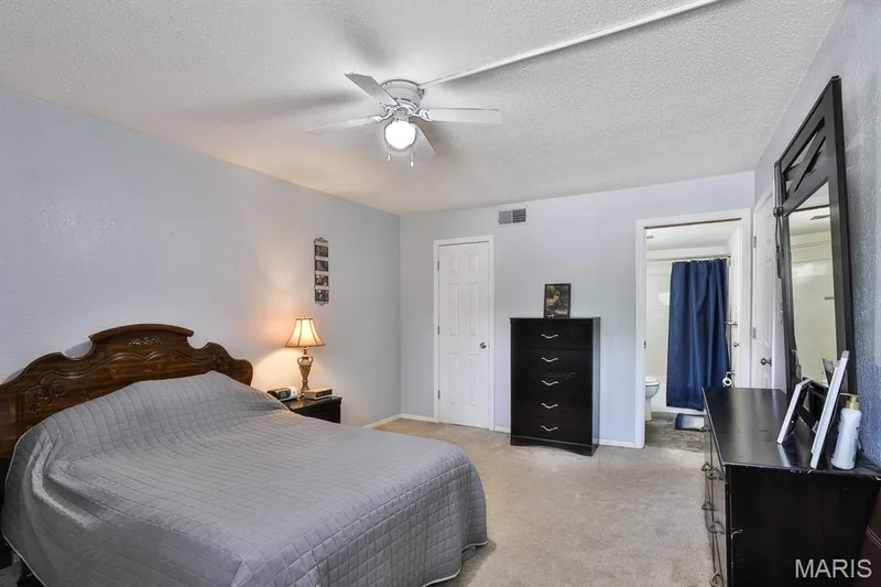 Bedroom with a textured ceiling, light colored carpet, ensuite bathroom, and a ceiling fan — 1380 Heritage Landing #206, St Charles, MO 63303