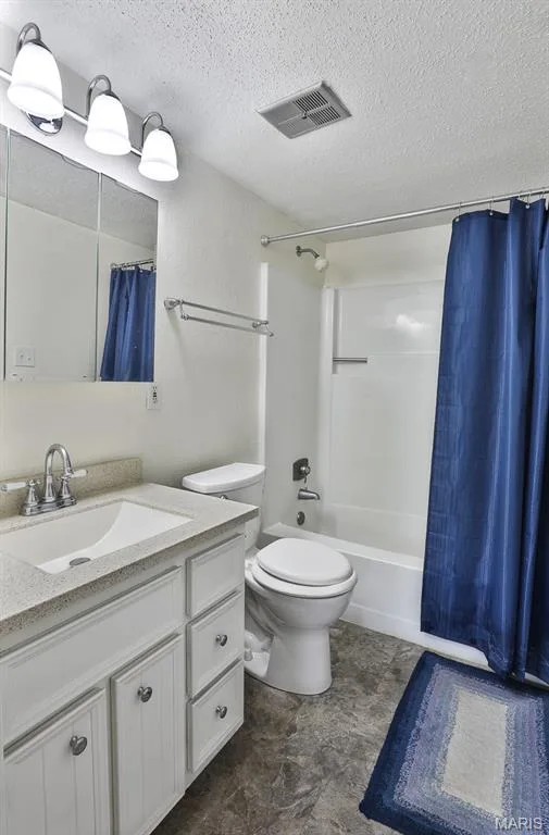 Full bathroom featuring a textured ceiling, vanity, and shower / tub combo with curtain — 1380 Heritage Landing #206, St Charles, MO 63303