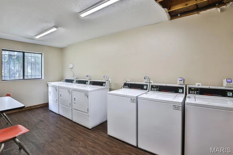 Communal laundry room featuring washer and dryer, a textured ceiling, and dark wood-style flooring — 1380 Heritage Landing #206, St Charles, MO 63303