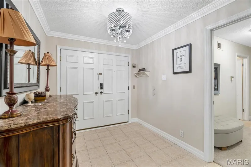 Foyer entrance featuring a chandelier, a textured ceiling, light tile patterned floors, and ornamental molding — 1511 Hampton Hall Drive #19 & 20, Chesterfield, MO 63017