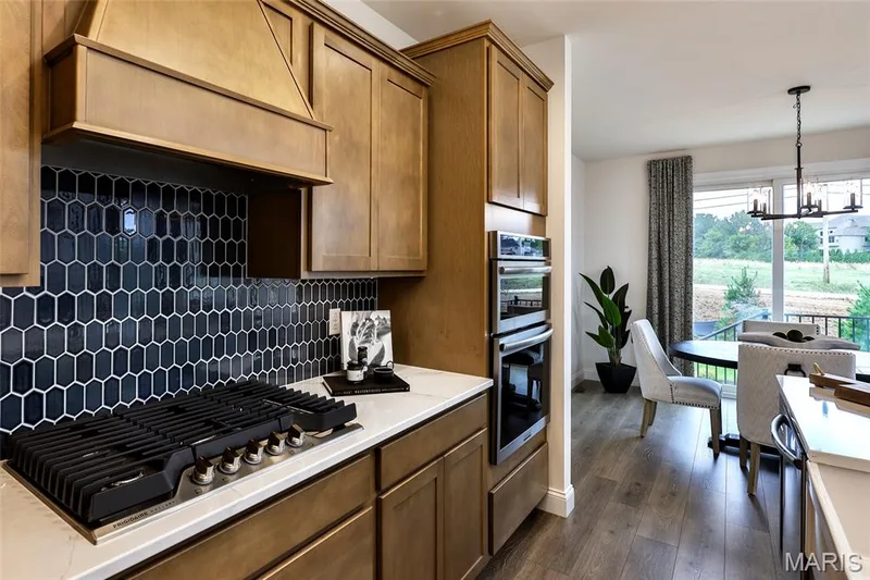 Kitchen featuring custom exhaust hood, a chandelier, appliances with stainless steel finishes, backsplash, and dark wood-style floors — 0 Braxton @ Montage at Hawk Ridge, Lake St. Louis, MO 63367