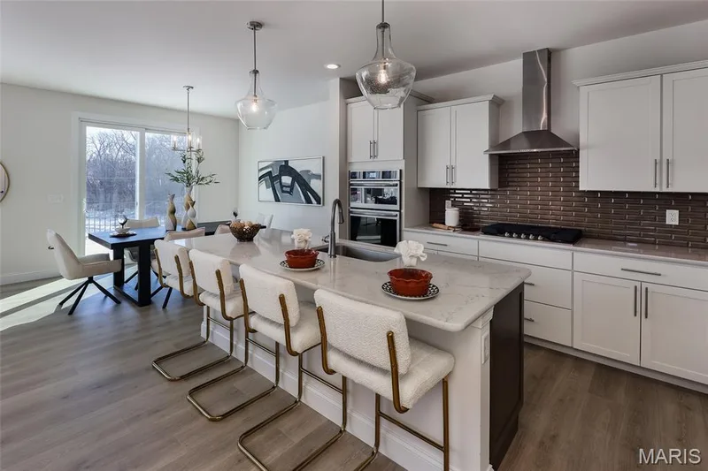 Kitchen with a breakfast bar, wall chimney range hood, decorative backsplash, white cabinets, and light stone counters — 0 Bridgeport - Montage at Hawk Ridge, Lake St. Louis, MO 63367