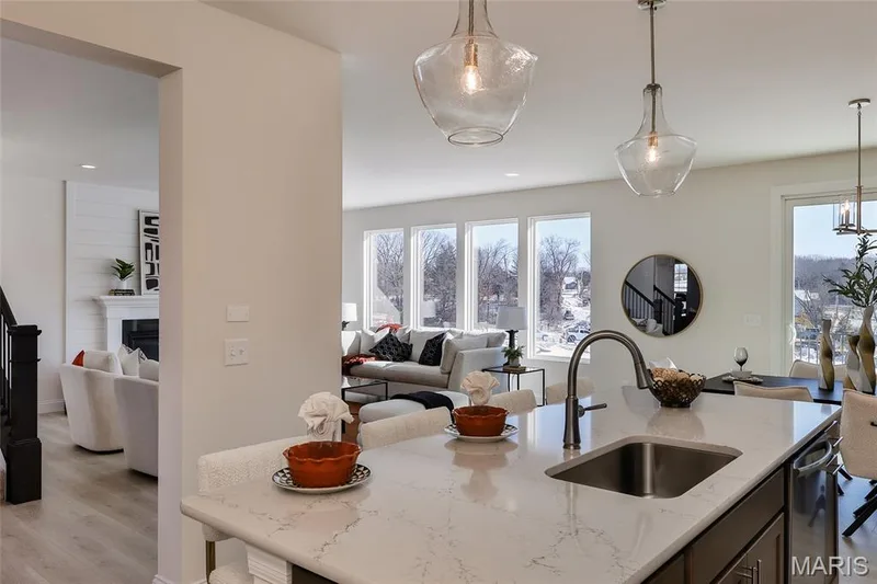 Kitchen with light wood-style flooring, hanging light fixtures, open floor plan, light stone counters, and a glass covered fireplace — 0 Bridgeport - Montage at Hawk Ridge, Lake St. Louis, MO 63367