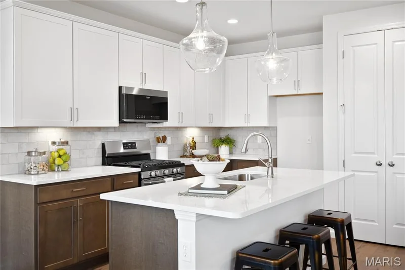 Kitchen with stainless steel appliances, a kitchen island with sink, white cabinetry, tasteful backsplash, and hanging light fixtures — 0 Chesapeake @ Montage at Hawk Ridge, Lake St. Louis, MO 63367