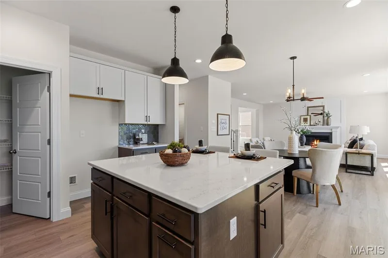 Kitchen featuring decorative light fixtures, light wood-type flooring, a lit fireplace, backsplash, and a kitchen island — 0 Lancaster @ Montage at Hawk Ridge, Lake St. Louis, MO 63367