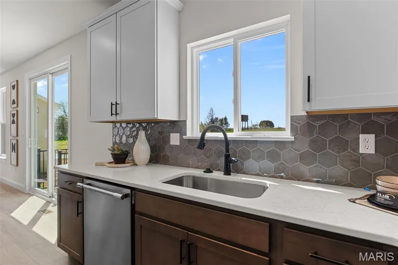 Kitchen with stainless steel dishwasher, tasteful backsplash, light stone counters, and healthy amount of natural light — 0 Lancaster @ Montage at Hawk Ridge, Lake St. Louis, MO 63367