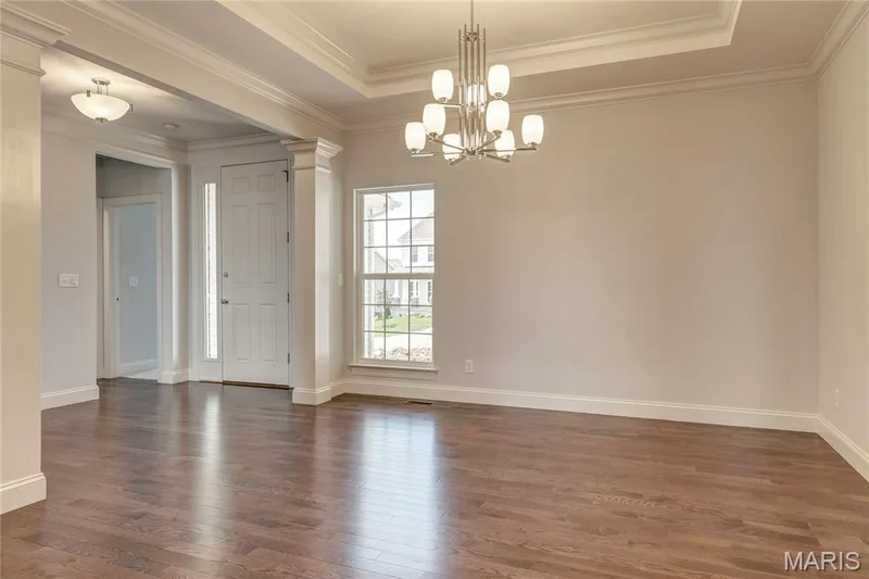 Unfurnished dining area featuring a tray ceiling, dark wood-type flooring, ornamental molding, a chandelier, and decorative columns — 0 Pierce @ Montage at Hawk Ridge, Lake St. Louis, MO 63367
