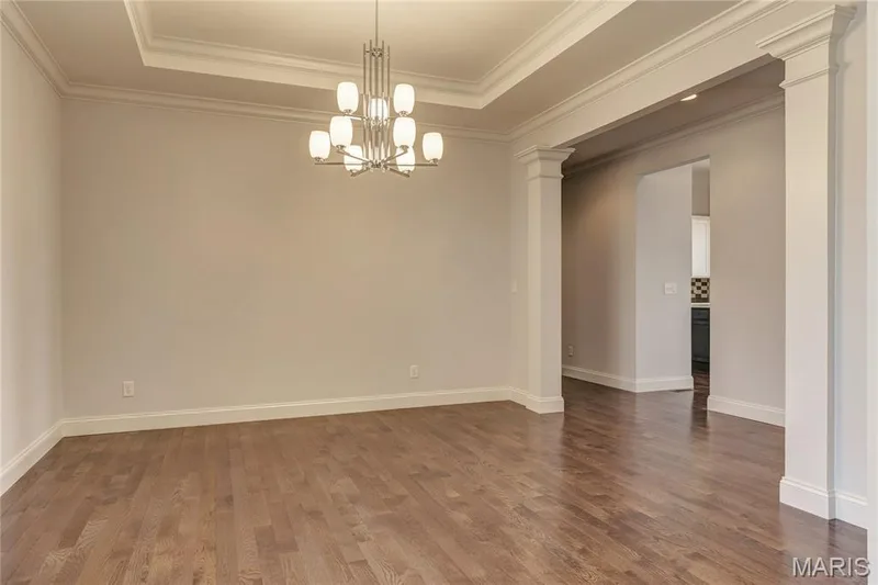 Spare room with a tray ceiling, dark wood-type flooring, ornamental molding, a chandelier, and decorative columns — 0 Pierce @ Montage at Hawk Ridge, Lake St. Louis, MO 63367
