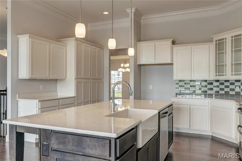 Kitchen with a center island with sink, white cabinetry, hanging light fixtures, light stone countertops, and ornamental molding — 0 Pierce @ Montage at Hawk Ridge, Lake St. Louis, MO 63367