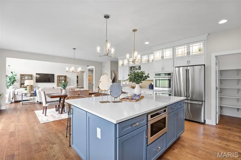 Kitchen with blue cabinets, glass insert cabinets, white cabinets, appliances with stainless steel finishes, and open floor plan — 2 Pin Oak at Hawk Ridge Estate, Lake St. Louis, MO 63367