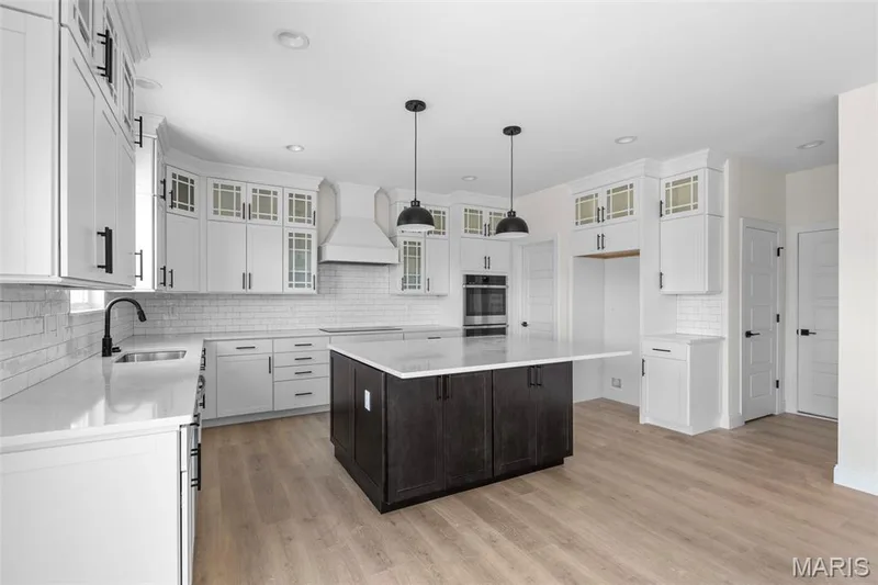 Kitchen with backsplash, white cabinets, custom exhaust hood, light wood finished floors, and a center island — 2 Sequoia at Hawk Ridge Estate, Lake St. Louis, MO 63367