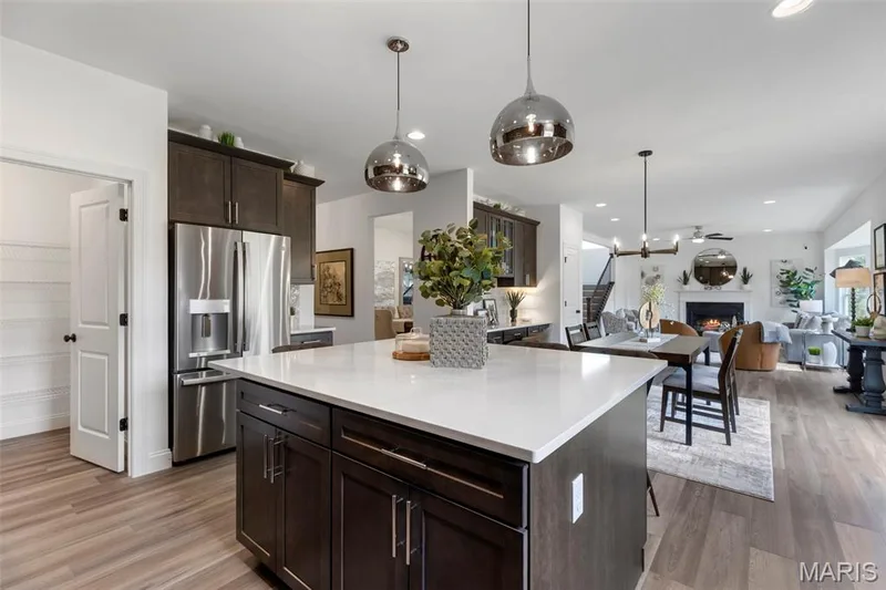 Kitchen featuring dark brown cabinets, stainless steel refrigerator with ice dispenser, pendant lighting, a warm lit fireplace, and a kitchen island — 2 Nottingham at Hawk Ridge, Lake St. Louis, MO 63367