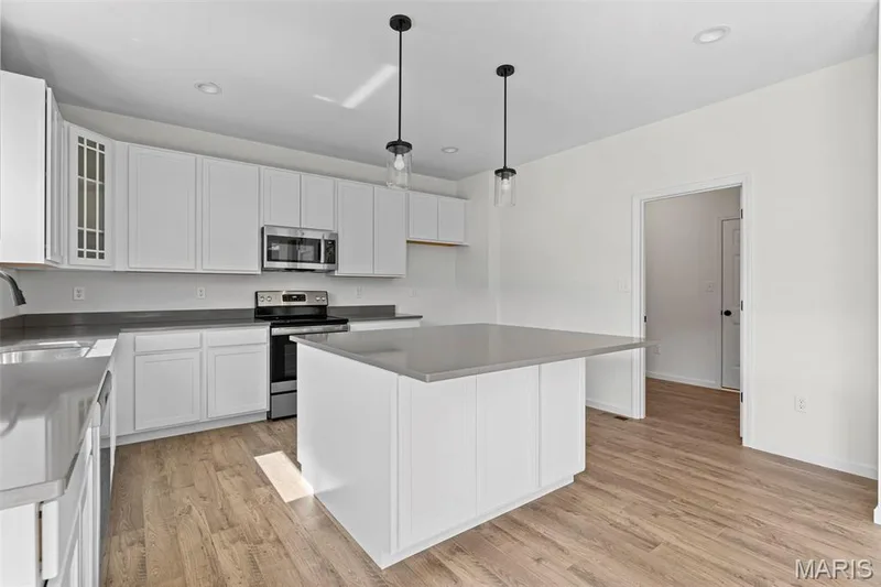 Kitchen featuring stainless steel appliances, a center island, white cabinetry, glass insert cabinets, and light wood-type flooring — 563 Edison Way, Wentzville, MO 63385