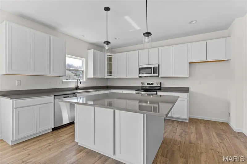 Kitchen featuring white cabinets, a kitchen island, pendant lighting, stainless steel appliances, and light wood-style flooring — 563 Edison Way, Wentzville, MO 63385