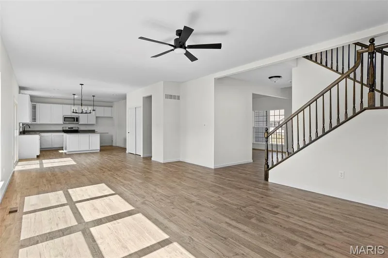 Unfurnished living room with light wood-style floors, stairs, a chandelier, and a ceiling fan — 563 Edison Way, Wentzville, MO 63385