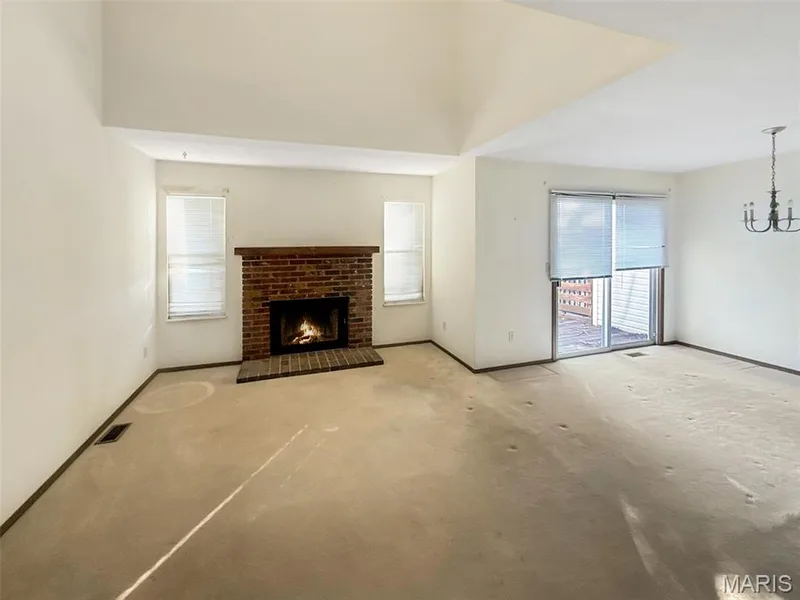 Unfurnished living room with a brick fireplace, carpet flooring, and a chandelier — 312 Crown Colony Court #F, St Peters, MO 63376