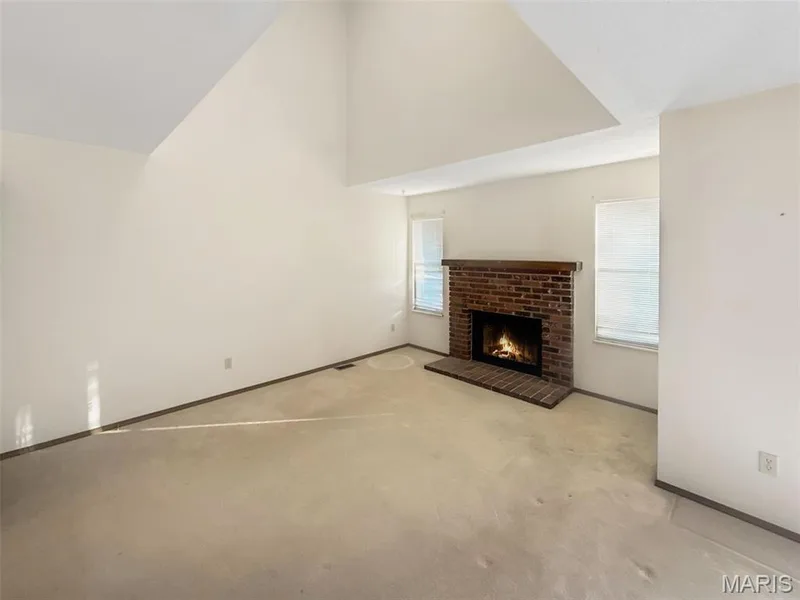 Unfurnished living room featuring a brick fireplace, carpet floors, and high vaulted ceiling — 312 Crown Colony Court #F, St Peters, MO 63376