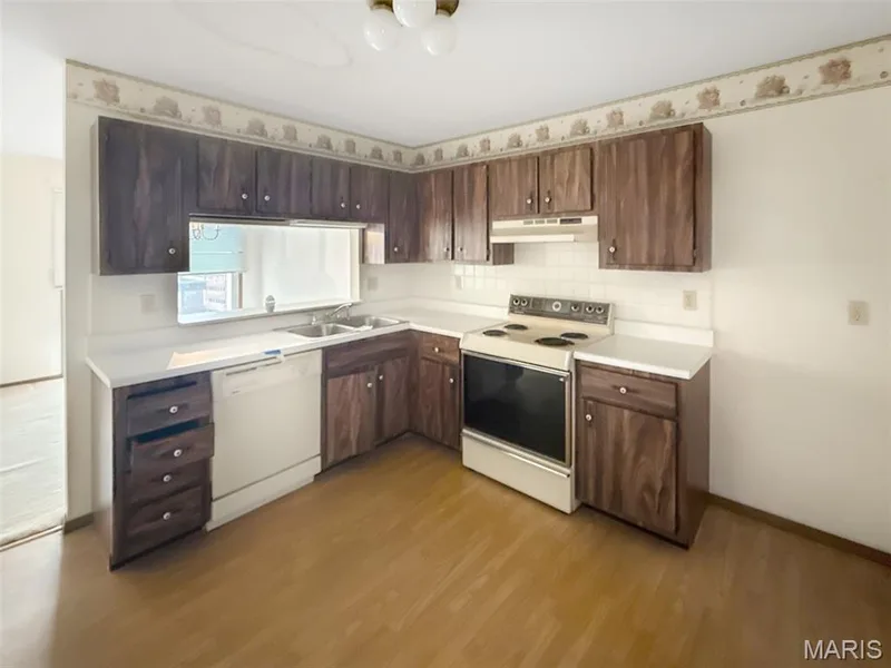Kitchen featuring white appliances, light countertops, dark brown cabinets, light wood-type flooring, and under cabinet range hood — 312 Crown Colony Court #F, St Peters, MO 63376