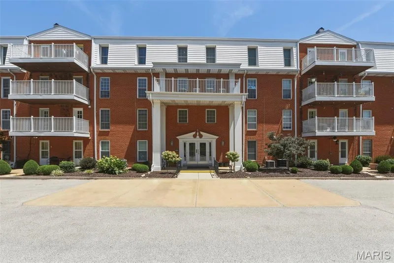 Brick exterior building featuring multiple balconies with white railings, a prominent covered entrance with white columns, and dormer windows on the upper level — 14443 Bantry Lane #16, Chesterfield, MO 63017