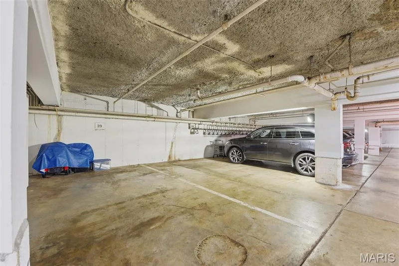 Dedicated parking space within a subterranean garage, featuring concrete flooring and exposed ceiling pipes — 14443 Bantry Lane #16, Chesterfield, MO 63017
