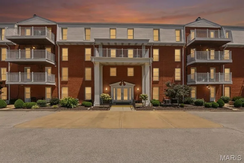 Brick facade building featuring multiple private balconies with white railings, a central portico entrance with columns, and mature landscaping — 14443 Bantry Lane #16, Chesterfield, MO 63017