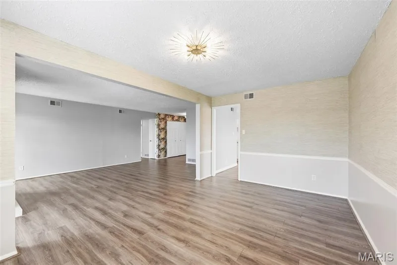 Spacious interior with wood-finish flooring, a contemporary ceiling light fixture, and textured wall coverings with wainscoting — 14443 Bantry Lane #16, Chesterfield, MO 63017