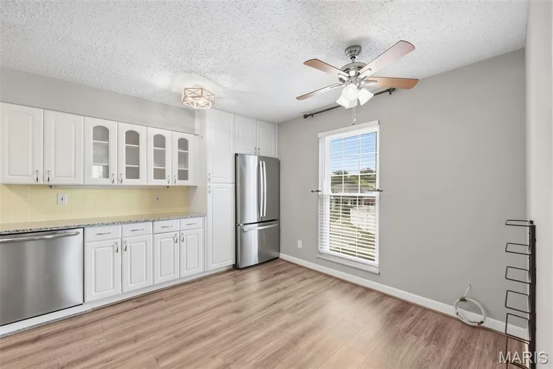 White cabinetry with glass-front accents, stainless steel appliances, wood-finish flooring, and a ceiling fan with integrated lighting — 14443 Bantry Lane #16, Chesterfield, MO 63017