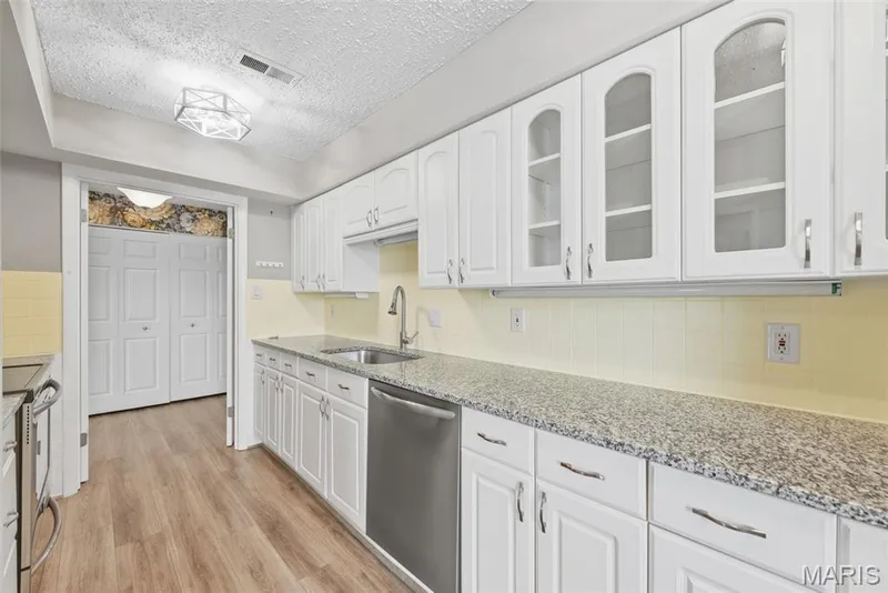 White cabinetry with glass-front uppers, speckled countertops, stainless steel sink, and wood-finish flooring — 14443 Bantry Lane #16, Chesterfield, MO 63017