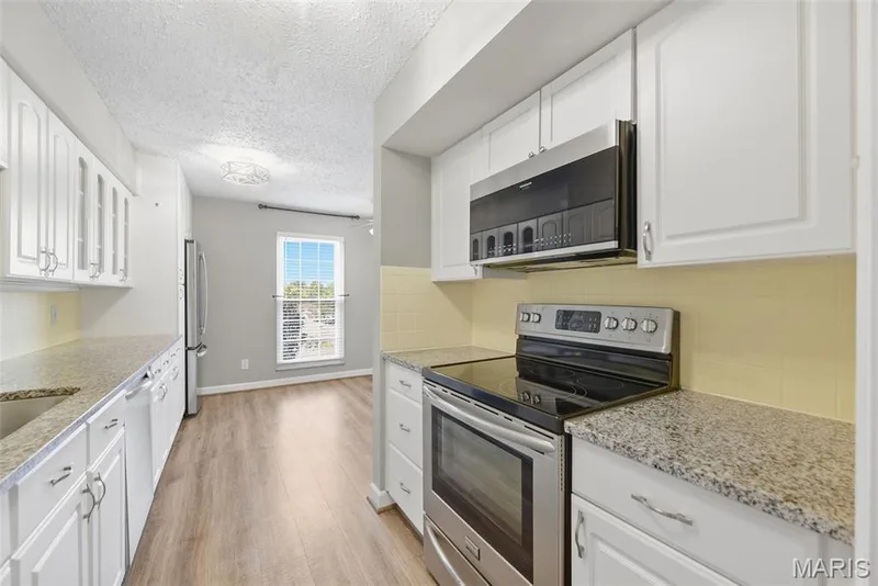Kitchen featuring white cabinetry, granite-style countertops, stainless steel appliances, and wood-finish flooring — 14443 Bantry Lane #16, Chesterfield, MO 63017