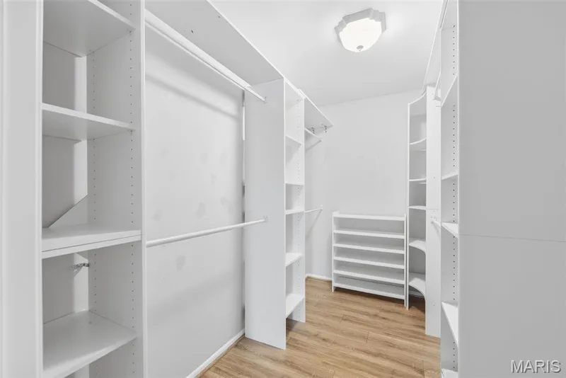 Walk-in closet with extensive white built-in shelving, hanging rods, and wood-finish flooring — 14443 Bantry Lane #16, Chesterfield, MO 63017