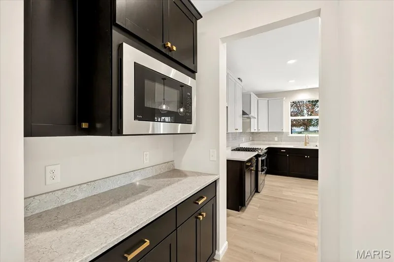 Kitchen Butlers Pantry with dark cabinets, light stone countertops, stainless steel appliances, tasteful backsplash, and light wood-style flooring — 210 Randlin Drive, O'Fallon, MO 63367