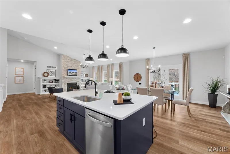 Kitchen with a stone fireplace, open floor plan, dishwasher, vaulted ceiling, and a center island with sink — 1 TBB Canterbury @ Kreder Farms, St Charles, MO 63304