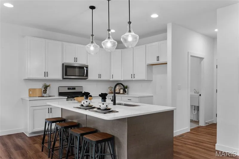 Kitchen with white cabinets, a breakfast bar, pendant lighting, dark wood finished floors, and a center island with sink — 1 TBB Rochester @ Kreder Farms, St Charles, MO 63304