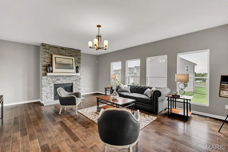 Living room with a fireplace, dark wood finished floors, and a chandelier — 1 TBB Sienna @ Kreder Farms, St Charles, MO 63304