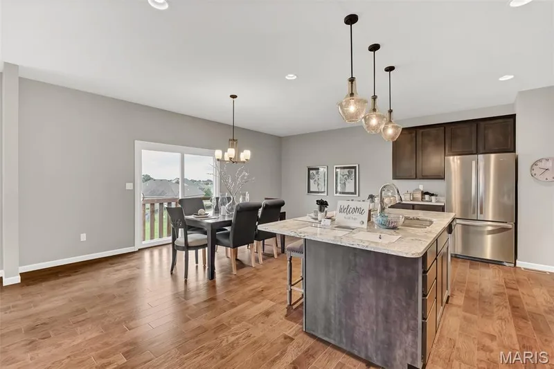 Kitchen with freestanding refrigerator, light stone counters, dark brown cabinets, a chandelier, and hanging light fixtures — 1 TBB Sienna @ Kreder Farms, St Charles, MO 63304