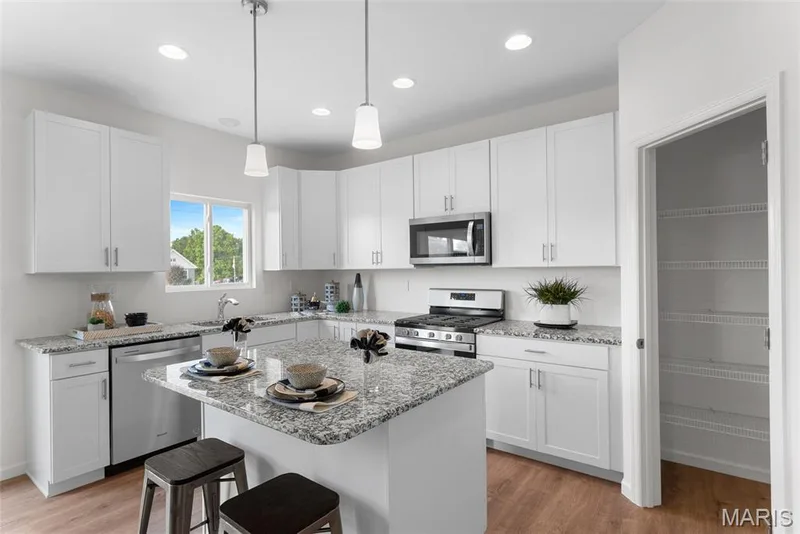 Kitchen featuring stainless steel appliances, white cabinets, light wood-style flooring, a breakfast bar, and a kitchen island — 1 TBB Barkley @ Kreder Farms, St Charles, MO 63304