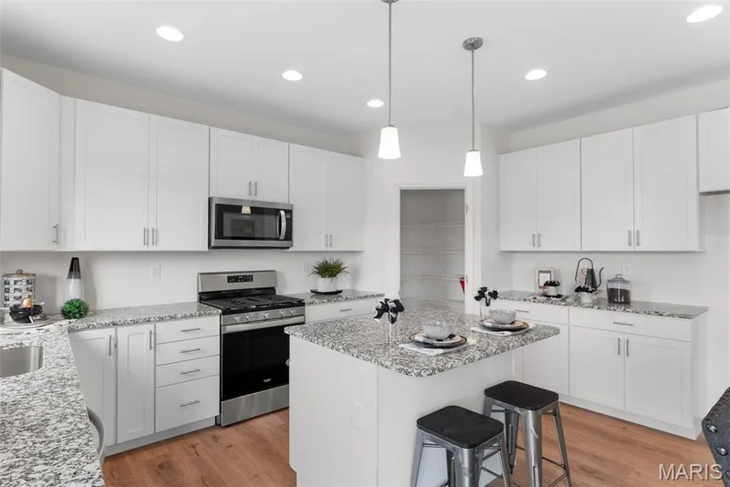 Kitchen with appliances with stainless steel finishes, a breakfast bar, white cabinets, light wood-type flooring, and pendant lighting — 1 TBB Barkley @ Kreder Farms, St Charles, MO 63304