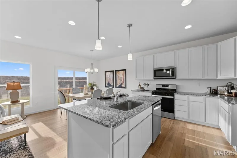 Kitchen featuring light stone countertops, white cabinetry, appliances with stainless steel finishes, a kitchen island with sink, and light wood-style flooring — 1 TBB Savoy @ Kreder Farms, St Charles, MO 63304