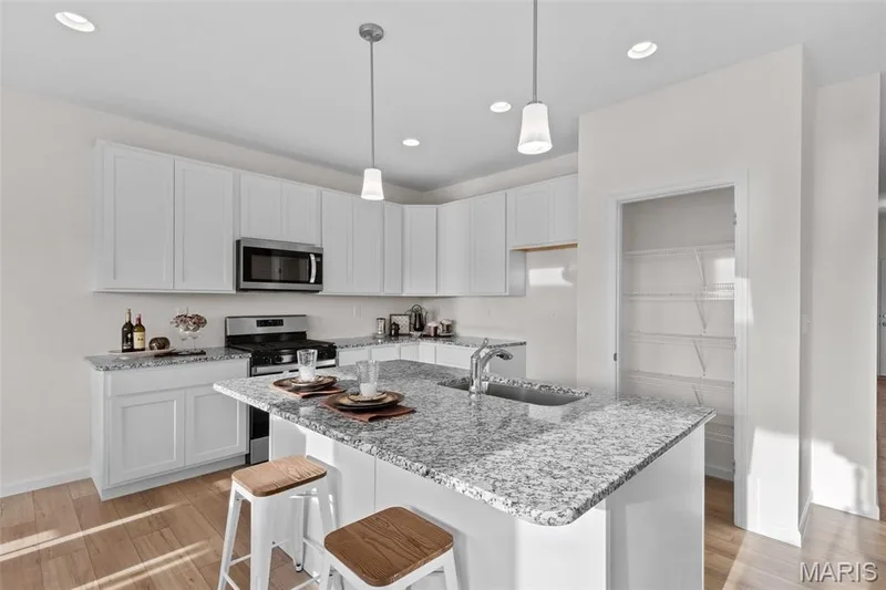 Kitchen featuring light wood finished floors, white cabinetry, light stone countertops, a kitchen breakfast bar, and recessed lighting — 1 TBB Savoy @ Kreder Farms, St Charles, MO 63304