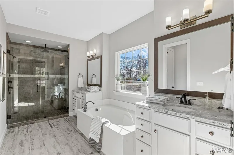 Bathroom featuring a bath, two vanities, a shower stall, and light wood-type flooring — 1 TBB Kingston @ Kreder Farms, St Charles, MO 63304